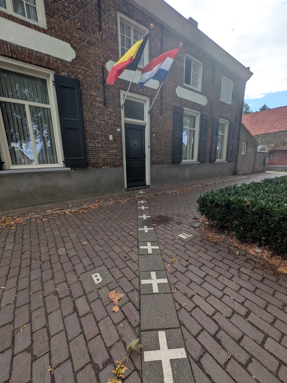 A street in Baarle with white cross-shaped border markers set into the pavement and both the Belgian and Dutch flags flying over the same house