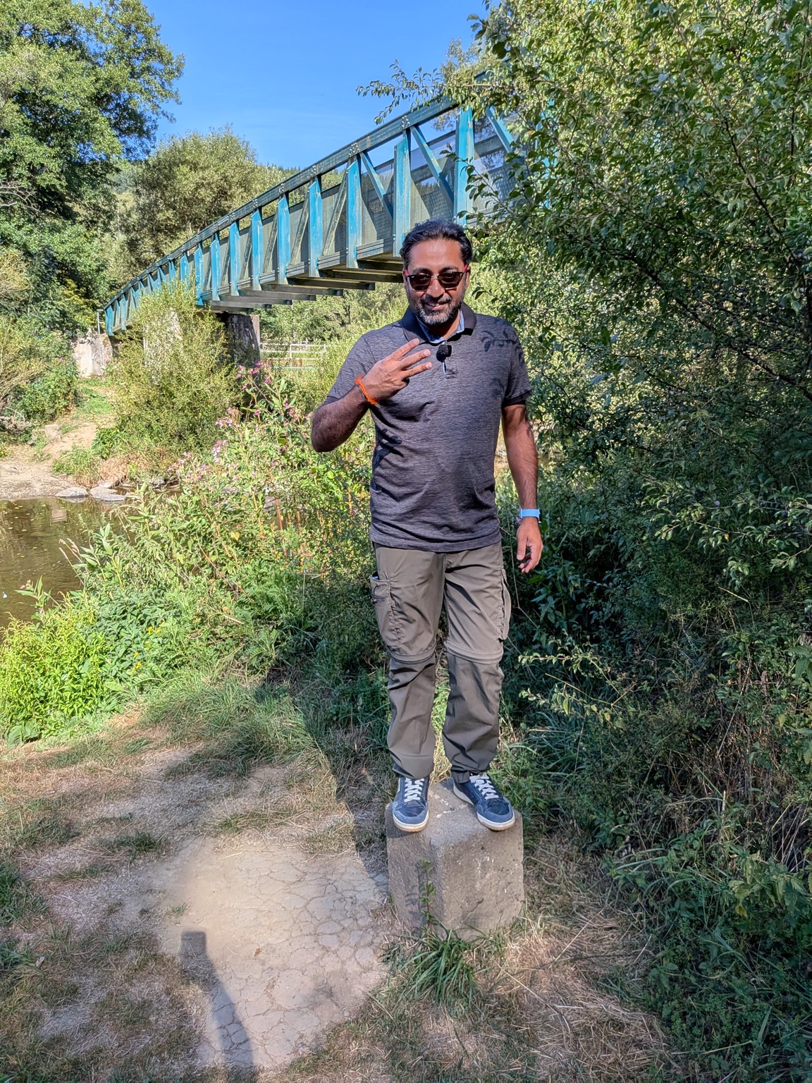 Standing on a boundary stone at the obscure Belgium, Luxembourg and Germany tripoint, with a footbridge over the Our river in the background