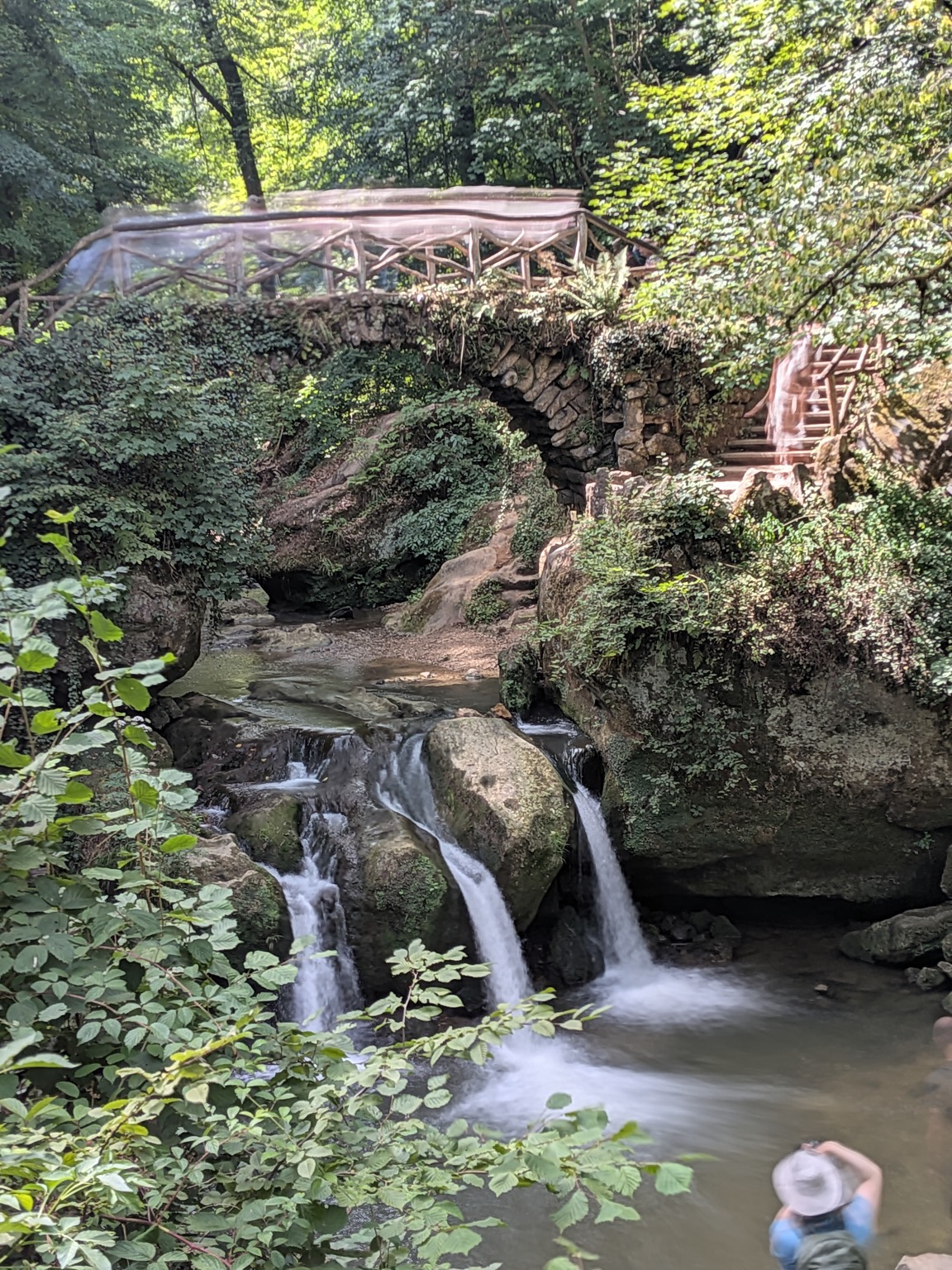 A three-tiered waterfall in the Mullerthal region of Luxembourg, with a wooden footbridge above it