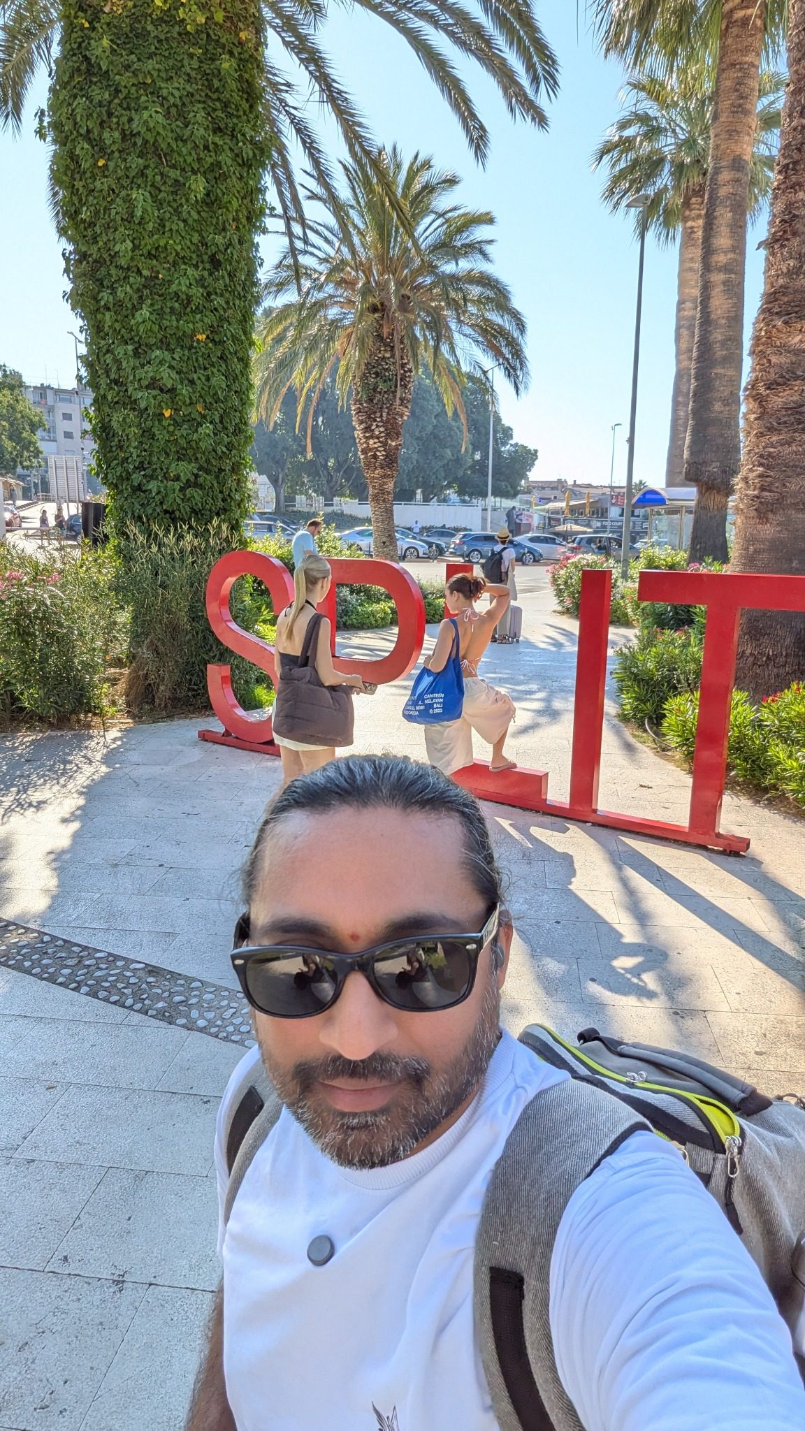 Saki The Wanderer at the red Split sign near the Riva waterfront with palm trees and blue sky